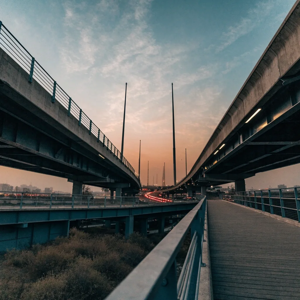 A multi-level Dubai highway interchange seen from a raking elevated angle at golden hour, with crossing concrete decks and bare lighting masts